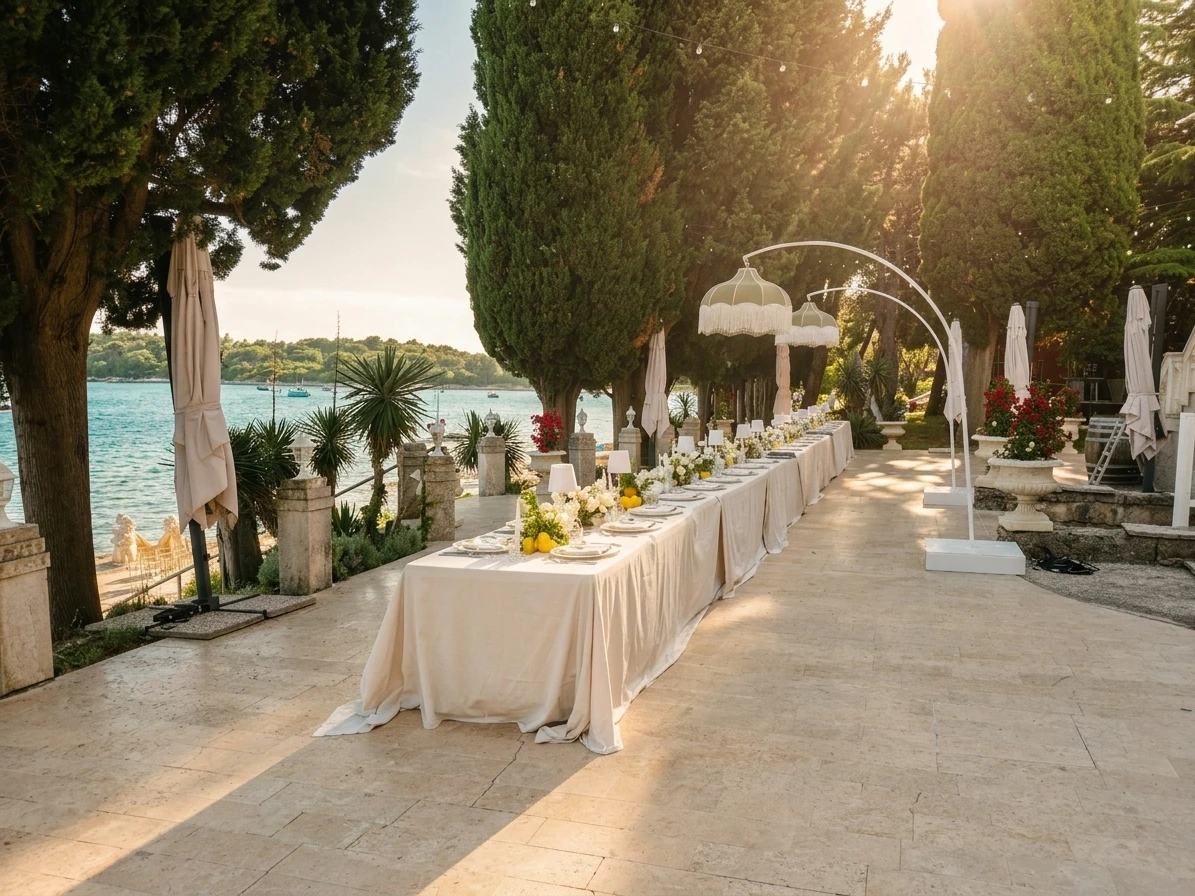 Eine lange Hochzeitstafel in elfenbeinfarbenem Leinen unter Zypressen am Meer, im goldenen Abendlicht
